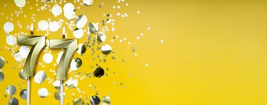 Yetmiş yedi yıllık doğum günü. 77 numaralı altın kutlama mumu. Sarı renkli arka plan. Doğum günü ya da yıldönümü kutlaması kavramı. Pankart. Boşluğu kopyala