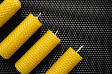 Siyah desenli balmumu arka planda duran dört sarı el yapımı mum. Üst Manzara. Düz yatıyordu