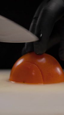 Mutfakta sebze doğrayan adam, yakın plan. Erkek eller plastik kesim tahtasıyla domatesleri keser. Dikey video