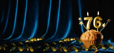 76 numaralı kutlama mumu ve parlak mavi kadife arka planda tatlı kek içinde küçük yıldızlar. Doğum günü ve yıldönümü kutlaması kavramı. Pankart. Boşluğu kopyala.