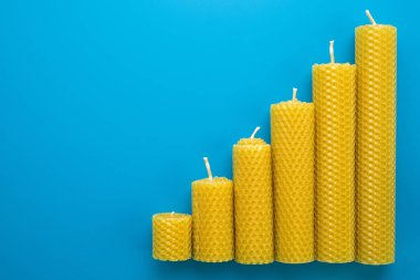 Balmumu mumları yükselen bir borsayı ya da kripto para birimini temsil etmek için yükselen sırayla dizilmiştir. Finansal büyümeyi sembolize eden canlı bir mavi arkaplan üzerine kurulmuş.