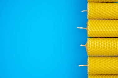 Sarı balmumu mumlar, canlı mavi bir arka planda dizilmiş, dokularını ve el yapımı cazibelerini sergiliyorlar. Doğal ürün ve el sanatları içeren temalar için mükemmel. Boşluğu kopyala