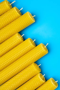 Sarı balmumu mumlar, parlak mavi bir arka planda düzgünce dizilmiş. Mumların altıgen dokusu görünür, doğal bileşimlerini vurguluyor. DIY ve hobi kavramı