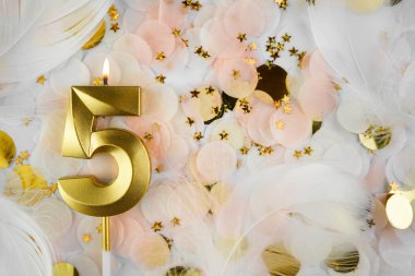 Beşinci Doğum Günü Kutlaması Altın Mum ve Konfeti ile. Pastel renkli konfeti, altın yıldız şekilleri ve beyaz tüy arkaplan arasında altın rakamlı beş doğum günü mumu..