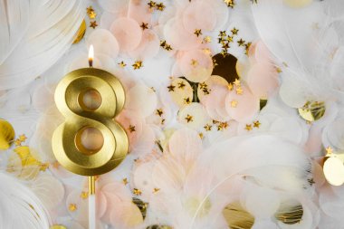 Altın Mum ve Konfeti ile Sekizinci Doğum Günü Kutlaması. Pastel renkli konfeti, altın yıldız şekilleri ve beyaz tüy arkaplan arasında altın rakamlı sekiz doğum günü mumu..