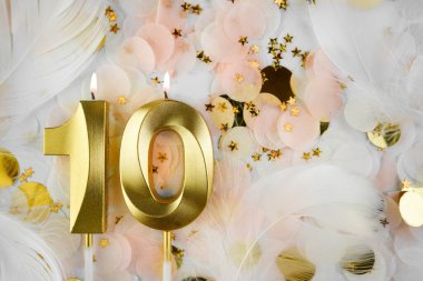 Altın Mum ve Konfeti ile Onuncu Doğum Günü Kutlaması. Pastel renkli konfeti, altın yıldız şekilleri ve beyaz tüy arkaplan arasında altın rakamlı on doğum günü mumu..