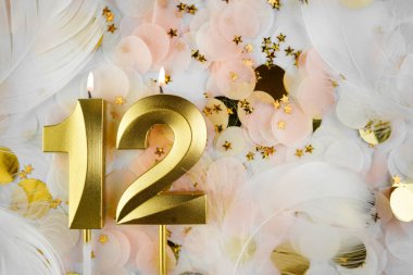 Altın Mum ve Konfeti ile 12. Doğum Günü Kutlaması. Pastel renkli konfeti, altın yıldız şekilleri ve beyaz tüy arkaplan arasında altın rakamlı on iki doğum günü mumu yakıldı..