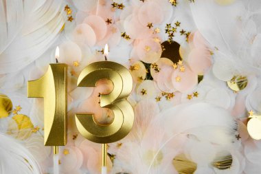 Altın Mum ve Konfeti ile 13. Doğum Günü Kutlaması. Pastel renkli konfeti, altın yıldız şekilleri ve beyaz tüyler arasında altın sayılı on üç yaş günü mumu yakıldı..