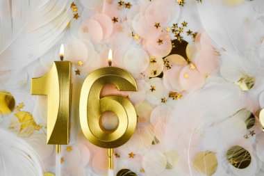 Altın Mum ve Konfeti ile 16. doğum günü kutlaması. Pastel renkli konfeti, altın yıldız şekilleri ve beyaz tüyler arasında altın rakamlı 16 yaş günü mumu..