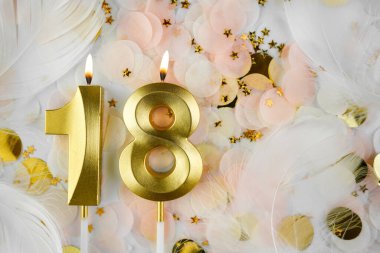 Altın Mum ve Konfeti ile 18. Doğum Günü Kutlaması. Pastel renkli konfeti, altın yıldız şekilleri ve beyaz tüy arkaplan arasında altın sayılı 18 yaş günü mumu..