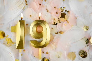 19. Doğum Günü Kutlaması Altın Mum ve Konfeti ile. Pastel renkli konfeti, altın yıldız şekilleri ve beyaz tüyler arasında altın sayılı on dokuz yaş günü mumu..