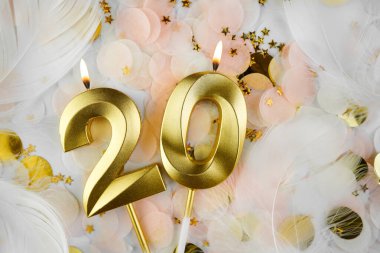Altın Mum ve Konfeti ile 20. doğum günü kutlamaları. Pastel renkli konfeti, altın yıldız şekilleri ve beyaz tüy arkaplan arasında altın rakamlı yirmi yaş günü mumu..