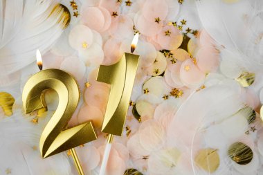 Altın Mum ve Konfeti ile 21. Doğum Günü Kutlaması. Pastel renkli konfeti, altın yıldız şekilleri ve beyaz tüyler arasında altın rakamlı 21 yaş günü mumu..