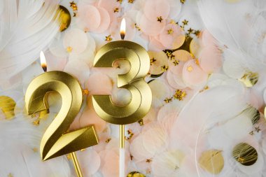 Altın Mum ve Konfeti ile 23. doğum günü kutlaması. Pastel renkli konfeti, altın yıldız şekilleri ve beyaz tüyler arasında altın rakamlı 23 yaş günü mumu..