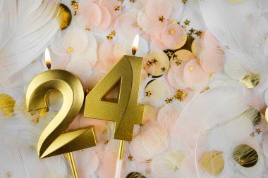 Altın Mum ve Konfeti ile 24. Doğum Günü Kutlaması. Pastel renkli konfeti, altın yıldız şekilleri ve beyaz tüyler arasında altın rakamlı 24 yaş günü mumu..