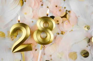 Altın Mum ve Konfeti ile 28. Doğum Günü Kutlaması. Pastel renkli konfeti, altın yıldız şekilleri ve beyaz tüyler arasında altın rakamlı 28 yaş günü mumu..