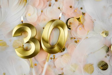 Altın Mum ve Konfeti ile 30 Doğum Günü Kutlaması. Altın rakamlı otuzuncu yaş günü mumu pastel renkli konfeti, altın yıldız şekilleri ve beyaz tüy arka planında yanar..