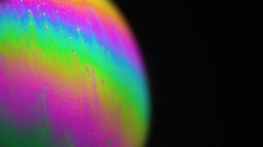 Makro renkli sabun köpüğü siyah arka plana karşı. Dönen yanardöner desen gerçeküstü ve kozmik bir görünüm yaratır, canlı renkleri vurgular..