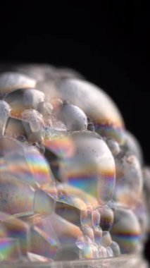 Sabun baloncuklarının yakın plan görüntüsü, siyah arka plana karşı karmaşık desenler ve yanardöner renkler sergiliyor. Doku ve yansıtıcı yüzeysel detaylar. Dikey video