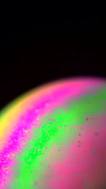 Renkli makro çekim sabun köpüğü yüzeyinde dönen şekilleri yakalıyor. Pembe, yeşil ve morun canlı tonları koyu bir arka plana karşı çarpıcı bir görsel etki yaratır. Dikey video