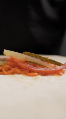 Adım adım shawarma tarifi. Şef, baharatlı Kore havucunun üzerine salatalık dilimleri koyarak sokak yemekleri hazırlıyor. Lezzetli sarmalar için taze malzemeler hazırlıyor..