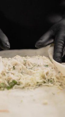 Şeflerin ellerinde siyah eldivenler, tavuk yahnisini ince lavaşla sarıyorlar. Adım adım shawarma tarifi. Fast food ve sokak mutfağı kavramı. Dikey video