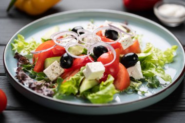 Taze sebze Yunan salatası. Kiraz domatesleri, kırmızı soğan, beyaz peynir ve ahşap masada mavi tabakta salatalık. Yakın plan.