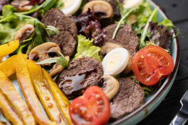 Sulu ızgara biftekli sıcak salata, kavrulmuş biber, topraksı mantarlar, taze sebzeler, haşlanmış yumurta ve keskin balzamik sos. Sağlıklı gurme yemeği. Kırsal bir geçmişi var. Yakın plan.