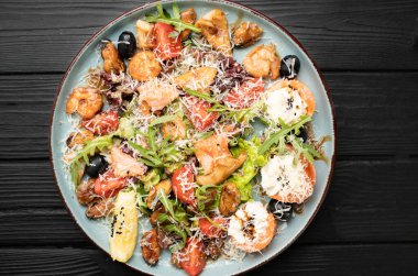 Izgara karides, midye, somon, krem peynir, parmesan peyniri, roka ve limon dilimleri içeren lezzetli deniz ürünleri salatası büyük bir tabakta büyük bir arkaplanda ustalıkla hazırlandı. Üst görünüm