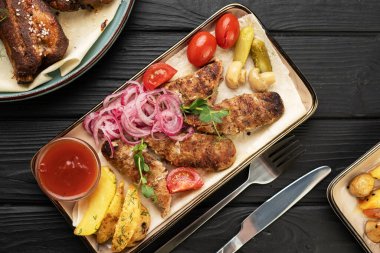 Geleneksel Türk mutfağından ızgara lula kebabı. Restoranda altın patates dilimleri, turşulu soğan, ızgara sebze, taze domates ve ahşap masada ketçap servis edilir. Üst görünüm