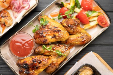 Taze domatesli ızgara tavuk kanadı ve beyaz tabakta ketçap, ahşap masa arkaplanı. Kızarmış kümes hayvanları, lezzetli fast-food ya da akşam yemeği, üst manzara. Boşluğu kopyala