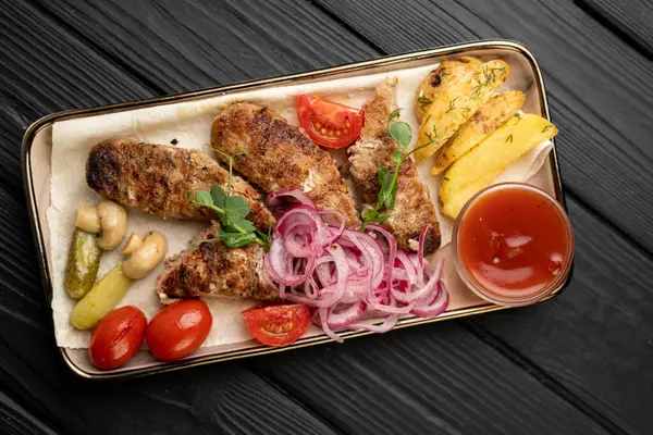 Otantik Türk yemekleri. Kızarmış patatesli ızgara şiş kebap, keskin ketçap, ızgara mantar, soğan turşusu ve ahşap masa üzerinde domates. Üst görünüm