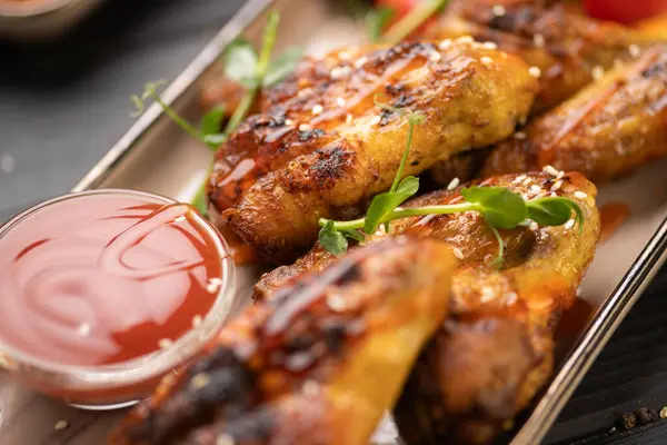 Ketçaplı kızarmış tavuk kanadı ve ahşap arka planda beyaz tabakta dilimlenmiş domates. Ev yapımı öğle yemeği, barbekü tarzı, kırsal masa sunumu. Boşluğu kopyala