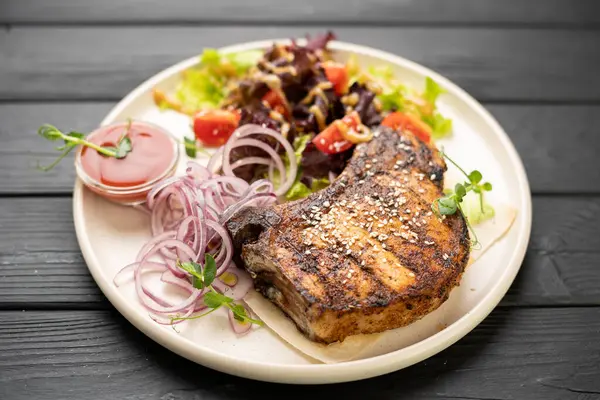 Izgara domuz bifteği, sebze salatası, marine edilmiş soğan ve tabakta vişneli domates. Lezzetli yemek, barbekü yemeği, restoran yemeği ve gurme yemeği kavramı..