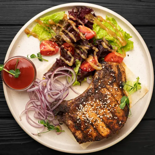 Salamura edilmiş kırmızı soğanlı sulu domuz eti, taze domates dilimleri ve yapraklı sebze salatası. Izgara et yemeği fikri. Lezzetli bir restoran tarzı sunum. Üst görünüm, yakın çekim