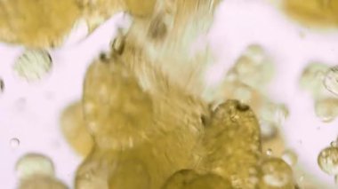 Altın yağ parlak beyaz arka planda suda kabarcıklar oluşturur. Yumuşak girdap dokusunun ve sıvı etkileşiminin makro yavaş çekim görüntüsü. Güzellik ya da soyut içerik için mükemmel.