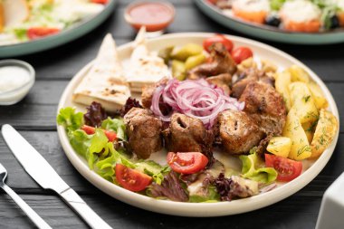 Kızarmış patates, taze domates, mor soğan ve lezzetli yemekler için kırsal ahşap masada gevrek marul yaprakları ile birlikte sunulan sulu domuz şiş parçaları..
