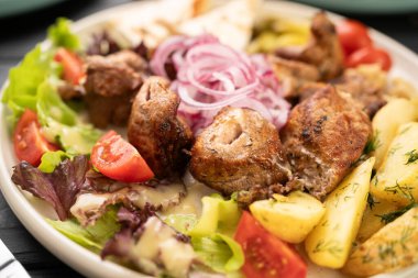 Lezzetli domuz eti ızgara patates, tatlı domates, mor soğan ve yaz eti festivali için ahşap panoda yapraklı marul karışımı. Yakın plan.