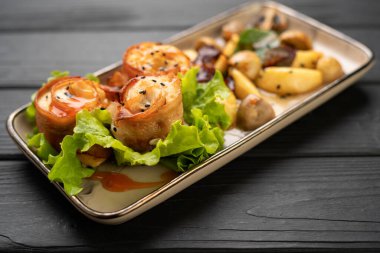 Domuz pastırmasına sarılı fırında tavuk eti patates ve marulla servis edilen rulo köfteler. Görünümün üstünde