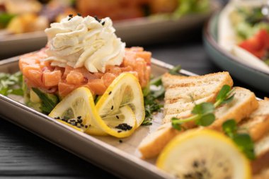 Krem peynir, limon dilimi ve siyah susam tohumuyla kaplı gurme somon ve avokado salatası. Kızarmış ekmek, zarif tabaklar, restoran tarzı taze yemekle servis edilir..