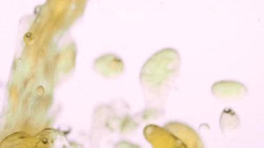 Altın yağ damlaları suyla birleşir, hassas kabarcıklar ve akışkan desenler oluşturur, sıvı doku ve ayrılma kavramı, yavaş makro video içinde akışkan hareket.