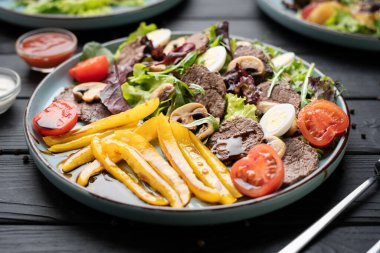 Biberli sıcak salata, biftek dilimleri, kiraz domatesleri ve restoran tabağında servis edilen bıldırcın yumurtaları.