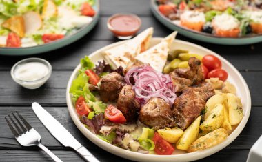 Lavaş ile doldurulmuş ızgara et suluguni peyniri, kızarmış patates, salata yaprakları ve soslar masada çatal bıçakla.