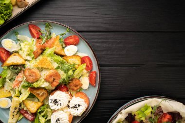 Kavurmalı sezar salatası, ızgara karides, kiraz domatesleri, yumurta, limon, parmesan ve somon suşi ruloları. Koyu ahşap masada servis ediliyor.
