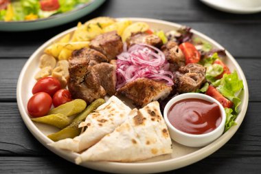 Izgara et kebabı, suluguni peyniri, vişneli domates, kızarmış patates, salatalık turşusu, ketçap ve soğanla doldurulmuş lavaşla servis edilir.