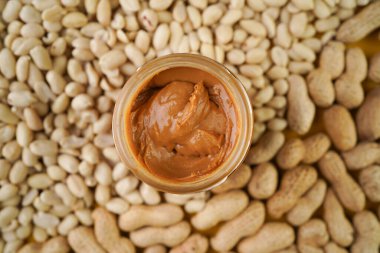 Fıstık ezmeli kavanozda fıstık ezmesi ve fındıklı arka plan, üst manzara, sağlıklı atıştırmalık. Boşluğu kopyala