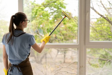 Profesyonel temizlik servisinin kadın çalışanı büyük bir apartmanın camlarını siler. Temizlik ve ev işleri kavramı