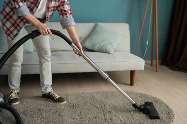 Kadın halıyı elektrikli süpürgeyle temizliyor. Temizlikçi halı süpürüyor. Ev rutini konsepti. Yakın plan.