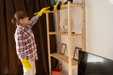 Bahar temizliği konsepti. Ev hanımı, toz bezi kullanarak raftan toz temizliyor. Kadın kitaplığı süpürüyor. Boşluğu kopyala