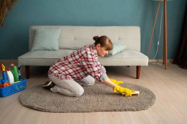 Orta yaşlı bir kadın evin oturma odasında fırçayla halı temizliyor. Ev işi ve temizlik konsepti